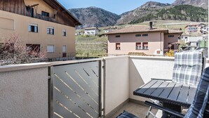 Un balcon avec une table et des chaises, un portail en métal et des bâtiments en arrière-plan.