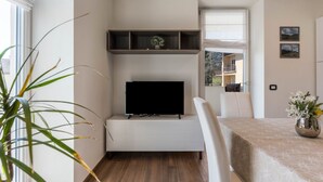 Ein modernes Wohnzimmer mit Flachbildfernseher, Essbereich mit Tisch und einem großen Fenster.