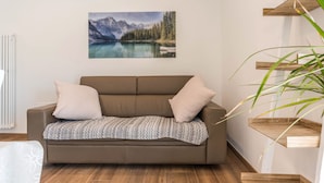 Ein modernes Wohnzimmer mit einem braunen Sofa, einem Gemälde von einer Berglandschaft und Holzregalen.