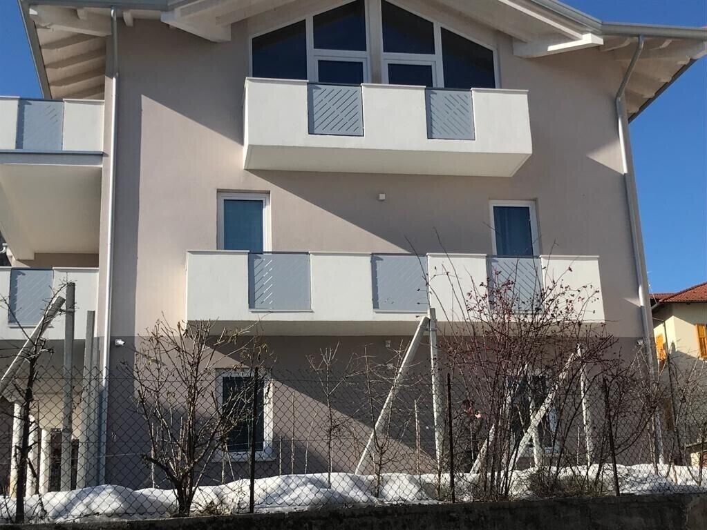 A multi-story building with balconies, a fence, and bare trees.