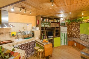 A kitchen with a wooden ceiling, a sink, a stove, and a dining area with stools.
