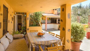 A covered patio with a table and chairs, a bowl of fruit, and potted plants. - Finca "La Alpispa" with Pool, Fast Wi-Fi, Terrace & Garden (Valleseco)