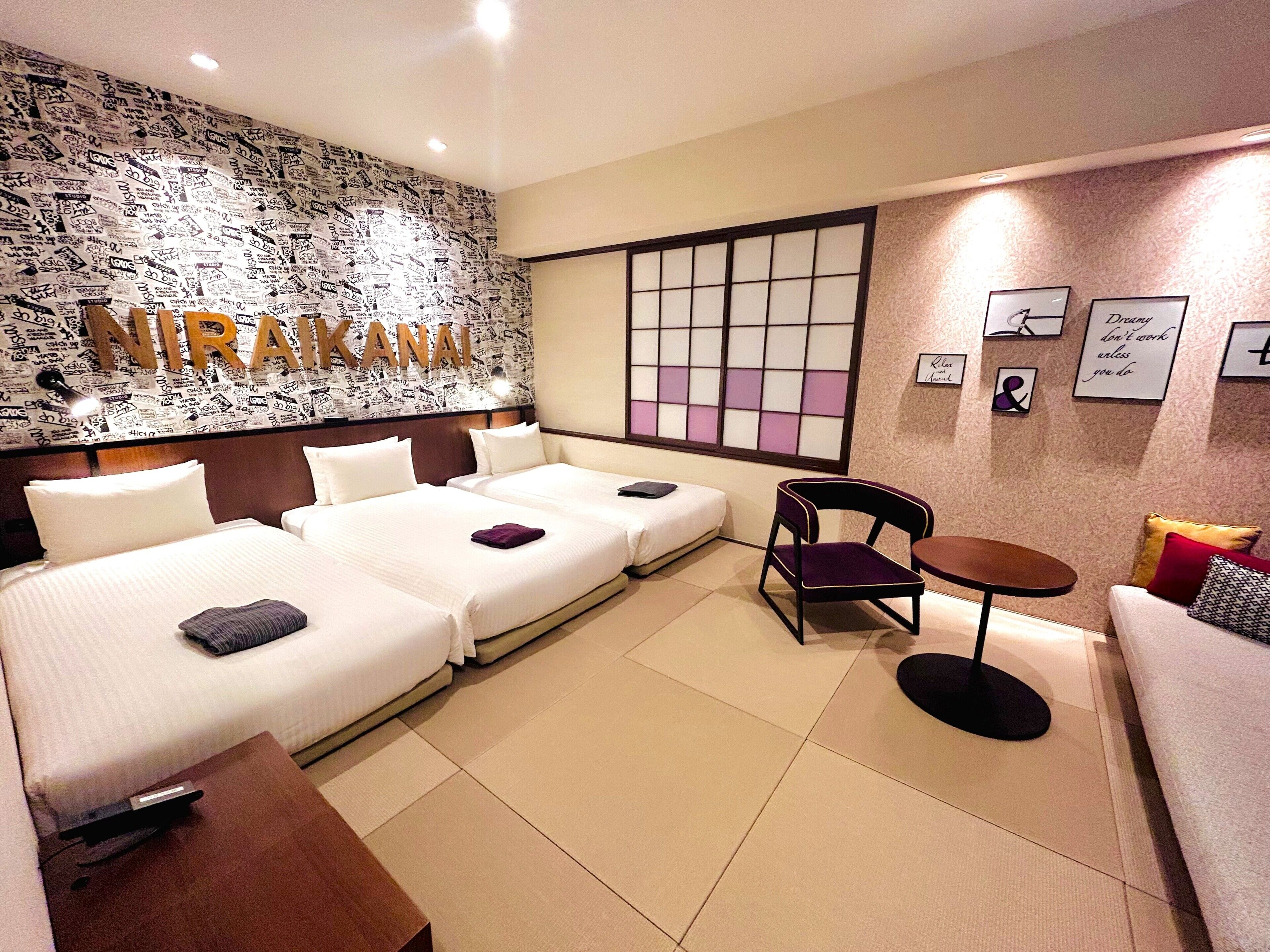 A hotel room with two beds, a sofa, a chair, a small table, and a decorative wall with a grid pattern and framed pictures.