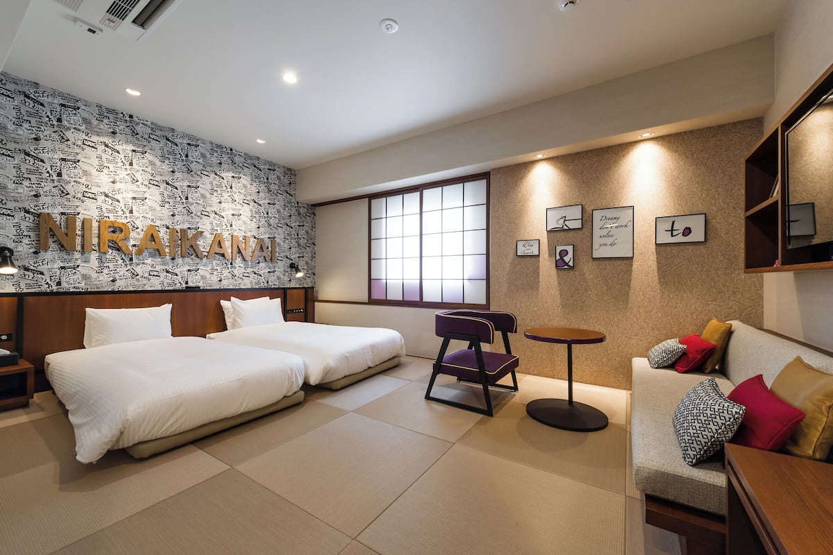 A hotel room with two beds, a sofa, a small table, and a wall with a name sign.