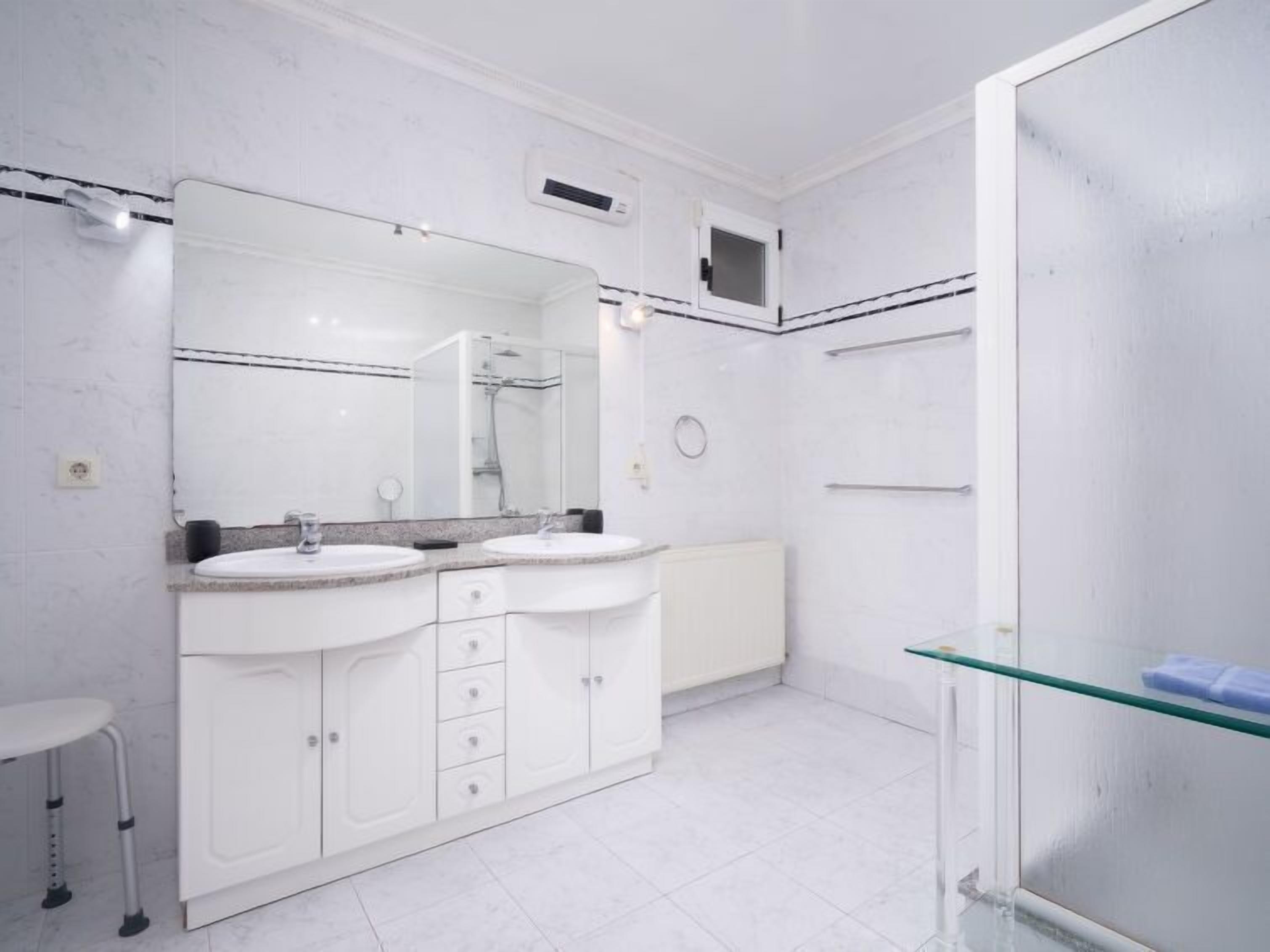 A modern bathroom with two sinks, a large mirror, and a glass shower enclosure.