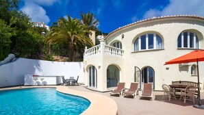 Un espace aménagé au bord de la piscine, avec une piscine aux formes arrondies, des chaises longues et une table à manger avec des chaises.