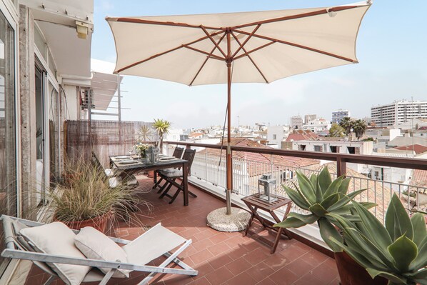 A balcony with a table, chairs, a large umbrella, and potted plants.