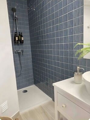 A bathroom with a shower, tiled walls, a sink, and a plant.