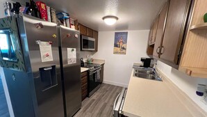 A compact kitchen with stainless steel appliances, wooden cabinets, a microwave, and a sink. - Rustic Girdwood Condo (Girdwood)