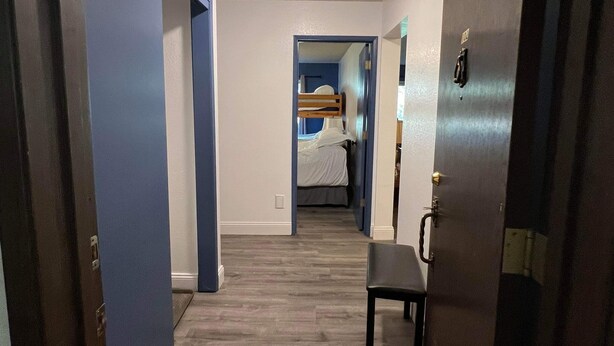 A narrow hallway with wooden flooring, a bed in the background, and a chair in the foreground. - Rustic Girdwood Condo (Girdwood)