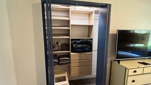 A room with a wooden floor, a wardrobe with multiple shelves, a small stool, and a television on a dresser. - Rustic Girdwood Condo (Girdwood)