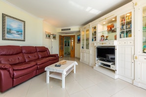 A living room with a red sofa, a coffee table, a TV, and a white cabinet with glass doors.