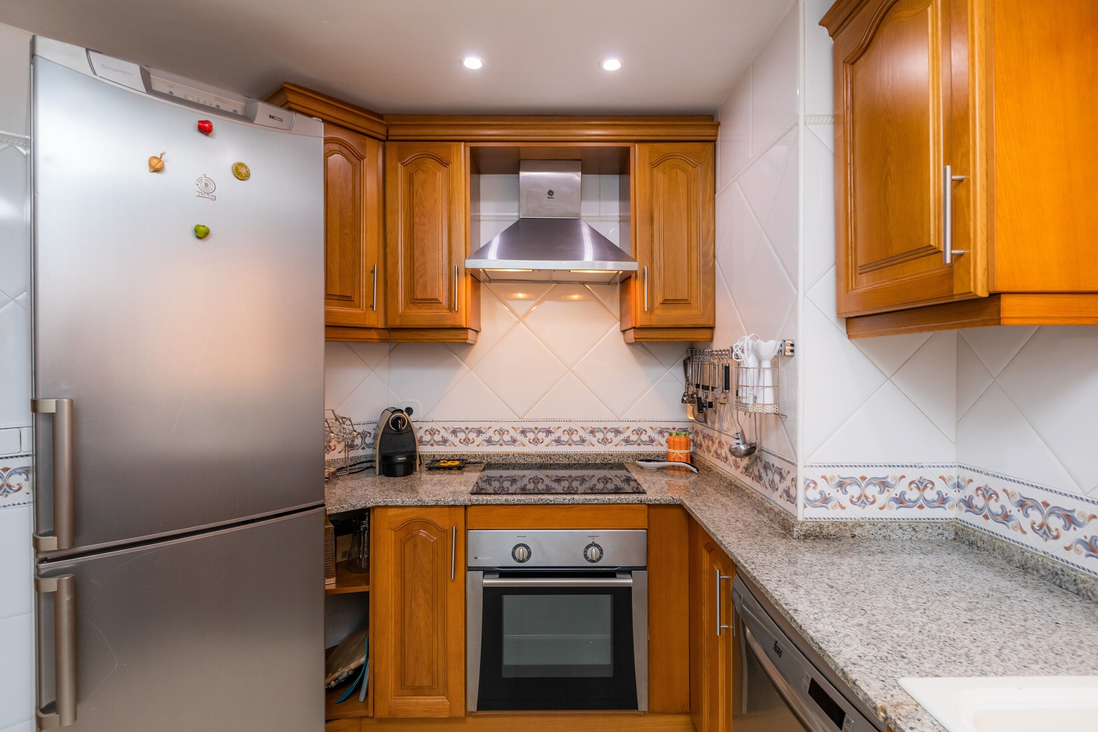 Una cocina con refrigerador de acero inoxidable, gabinetes de madera, estufa a gas y microondas.