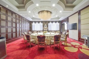 A conference room with a round table, chairs, a chandelier, and a red carpet.