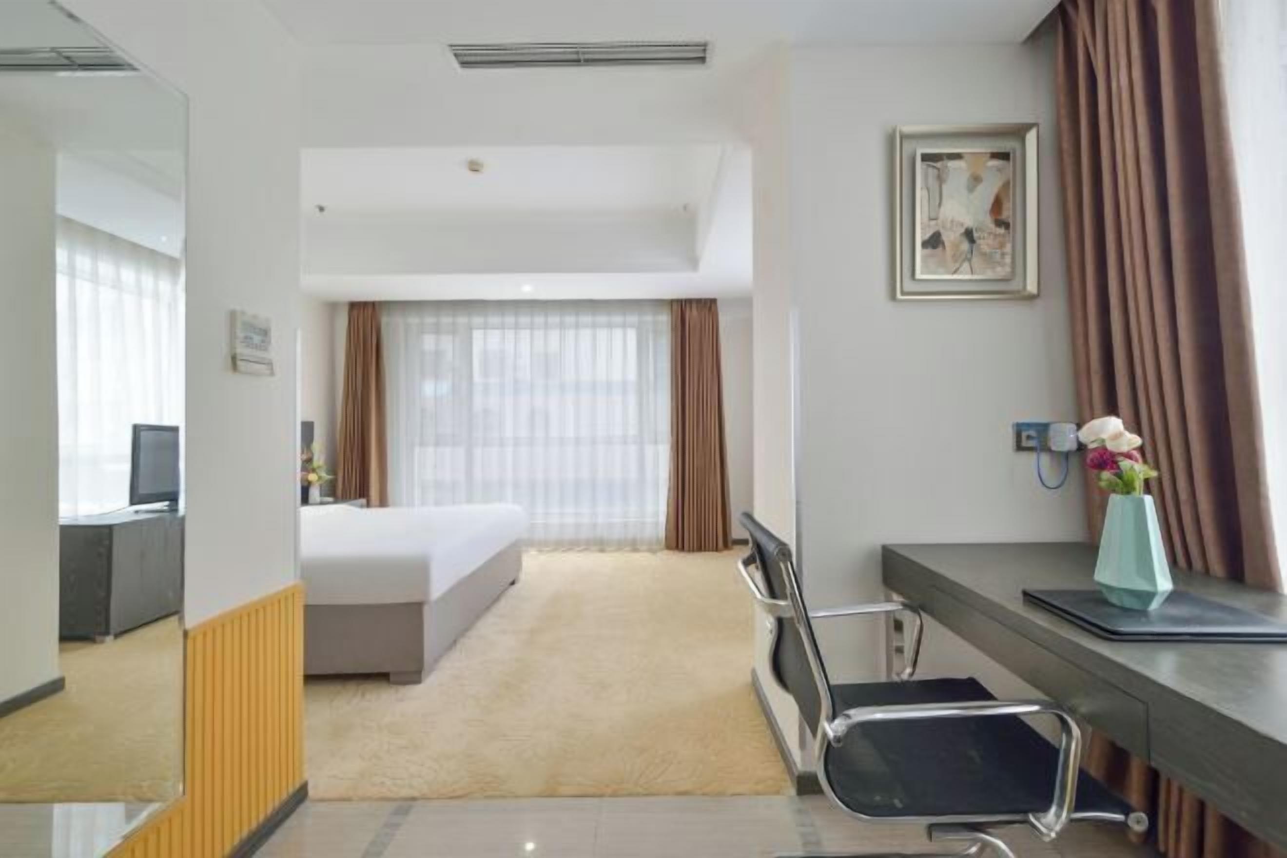 Habitación de hotel con cama, escritorio, silla, una mesita con un jarrón de flores y un cuadro en la pared.