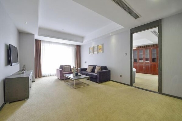 Una habitación de hotel moderna con sofá, mesa de centro y televisor sobre un soporte.