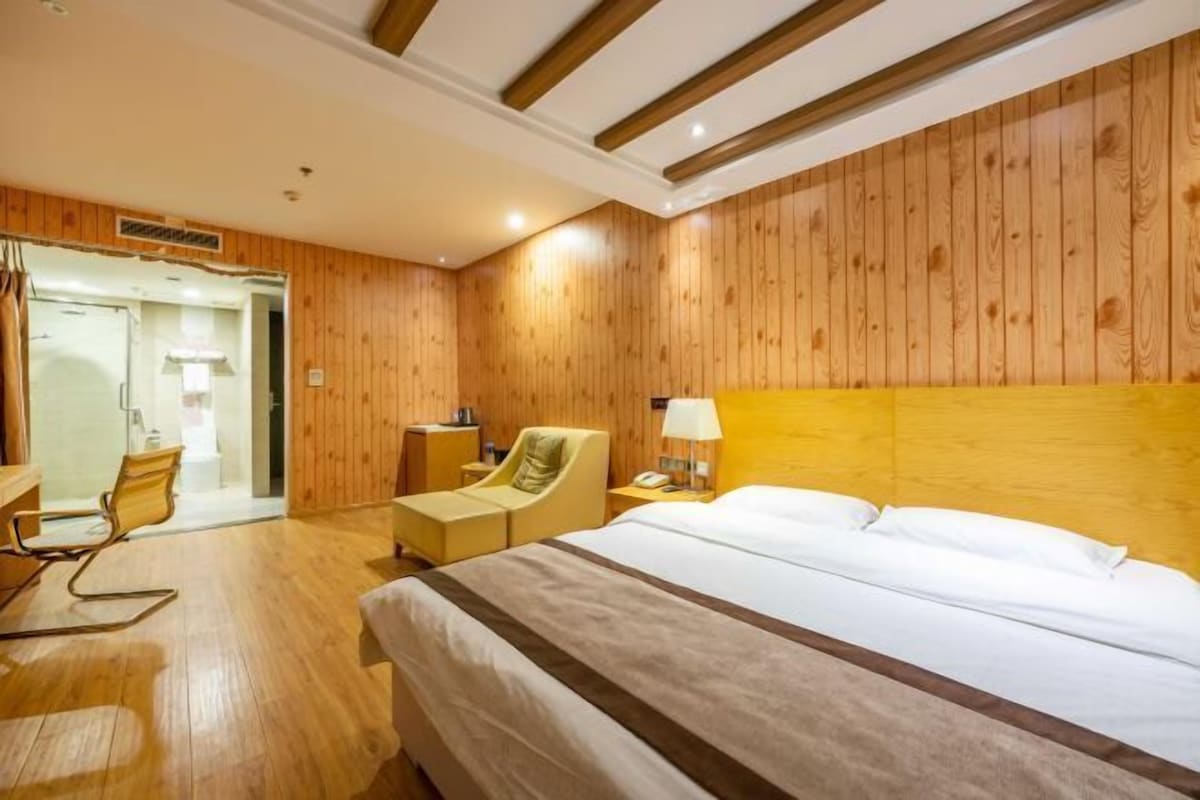 Habitación de hotel con paneles de madera, cama con ropa blanca, escritorio con silla y mesita de noche con lámpara.