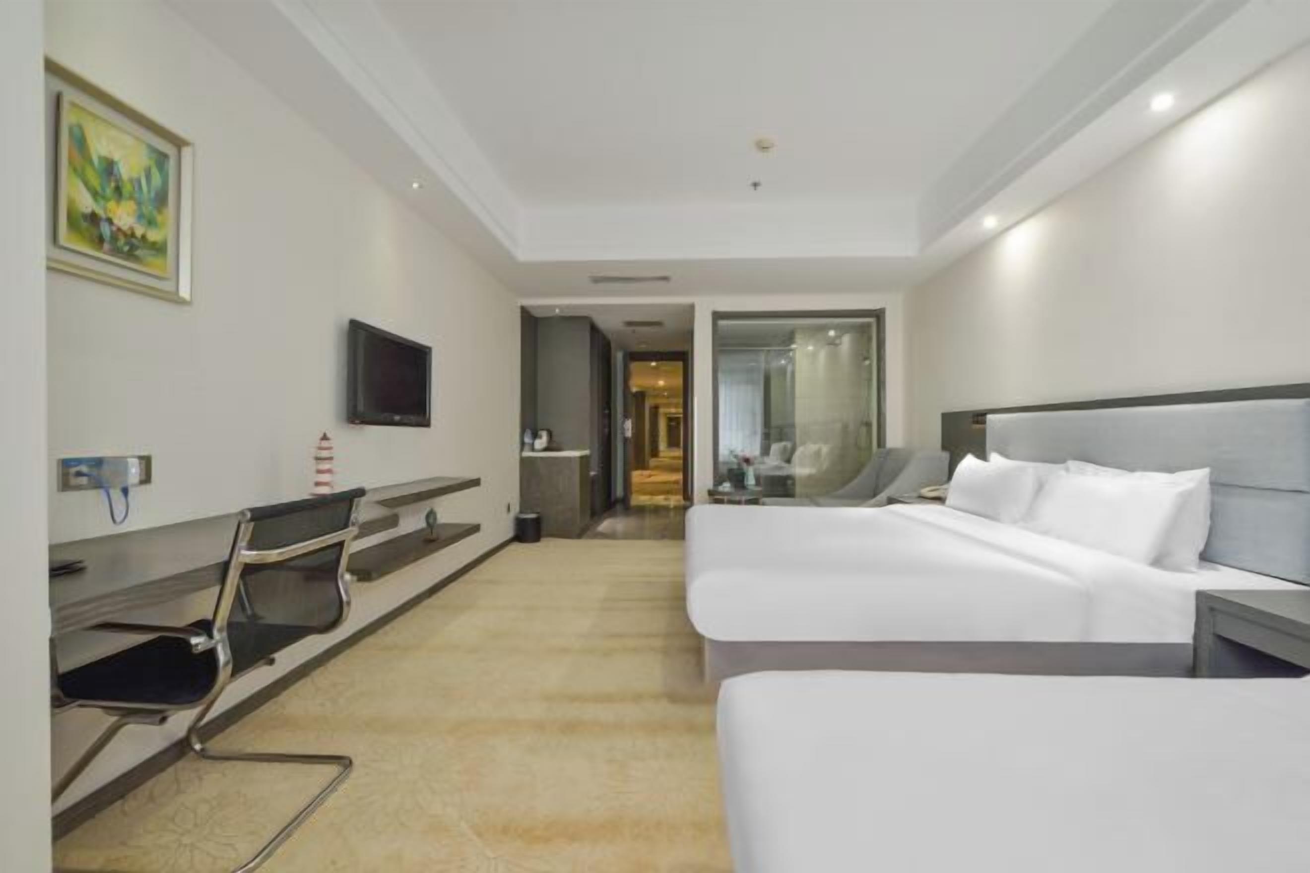 A hotel room with a bed, a desk, a chair, a TV, and a painting on the wall.