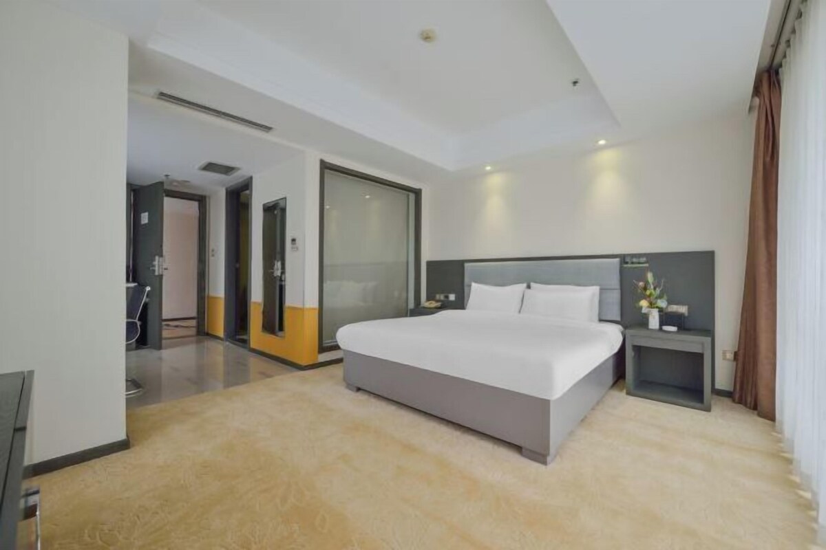 Una habitación de hotel moderna con una cama grande, una mesita de noche y vistas al pasillo.