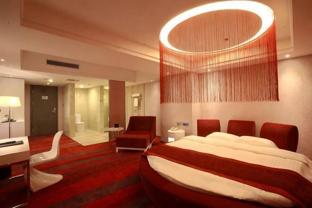 Une chambre d’hôtel avec un grand lit, un bureau, une chaise, un luminaire rond et un miroir.