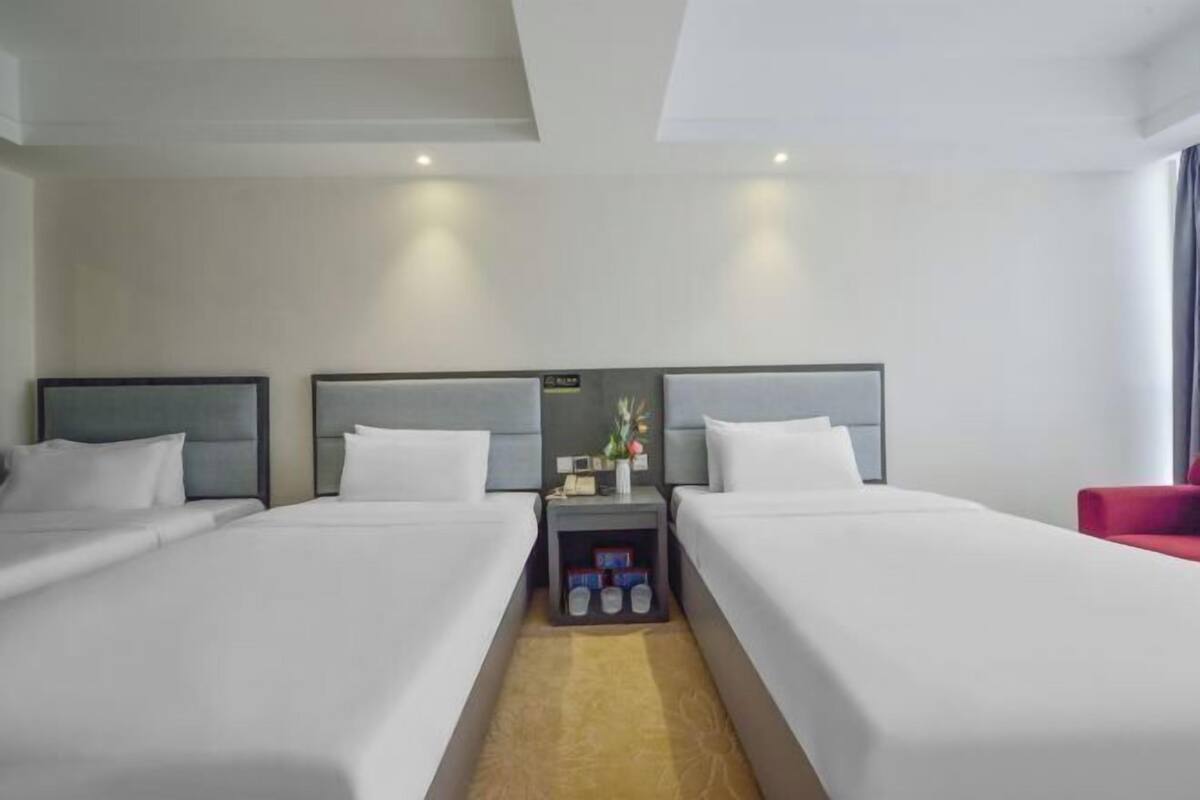 Une chambre d’hôtel avec deux lits, une table de chevet avec une lampe et un fauteuil rouge.