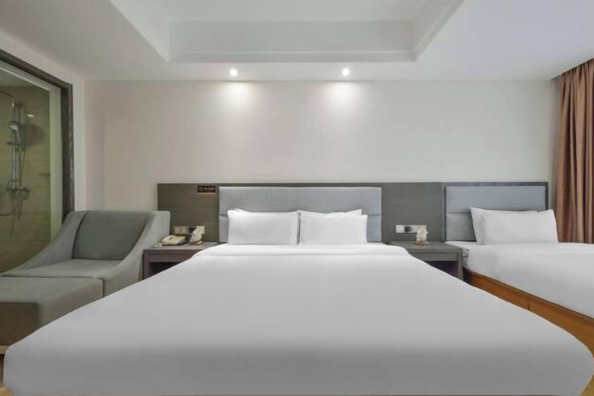 Une chambre d’hôtel avec un grand lit, deux tables de chevet, une commode, un coin salon et un espace douche.