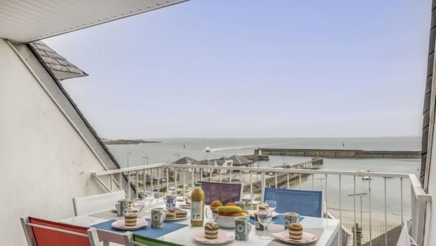 Un balcon avec une table préparée pour le petit-déjeuner, donnant sur une zone côtière avec une jetée.