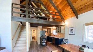 Une cuisine spacieuse avec des meubles de rangement en bois, un coin repas avec une table et des bancs en bois, et un escalier menant à un niveau supérieur.