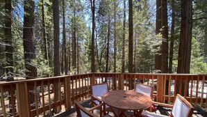 Une terrasse en bois avec une table ronde et quatre chaises, entourée de grands arbres.