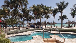 A pool area with a stone border, palm trees, and beach umbrellas.