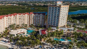 A resort with multiple buildings, a central pool, and a beach area with umbrellas.