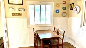 A dining area with a wooden table and chairs, a window with blinds, and wall decorations including signs reading "Café" and "Bistro".
