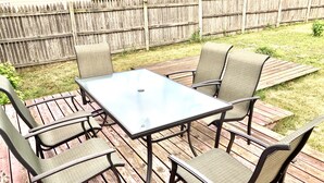A wooden deck with a glass-top table and four chairs.