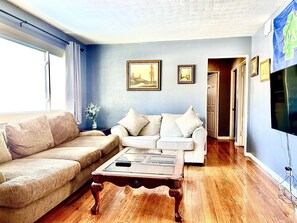 A living room with a beige sofa, a white sofa, and a wooden coffee table. There are two framed pictures on the wall, and a TV mounted on the wall. - 5 bedroom 2 bath house, walk to Notre Dame, safe area (South Bend)