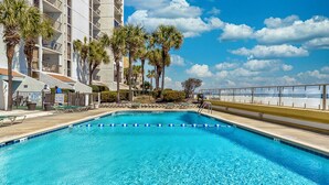 A swimming pool with clear blue water, surrounded by palm trees and a building with balconies. - Oceanfront 5th floor,quiet,peaceful.beautiful views (Myrtle Beach)
