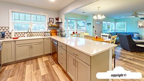 Cozinha moderna com uma ilha grande, piso de madeira e sala de jantar com sofá azul e mesa de centro.