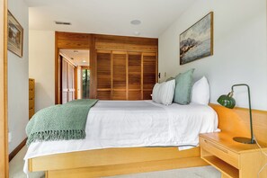 Una camera da letto con una struttura letto in legno, biancheria da letto bianca, una coperta verde, un comodino con una lampada e un quadro appeso al muro.