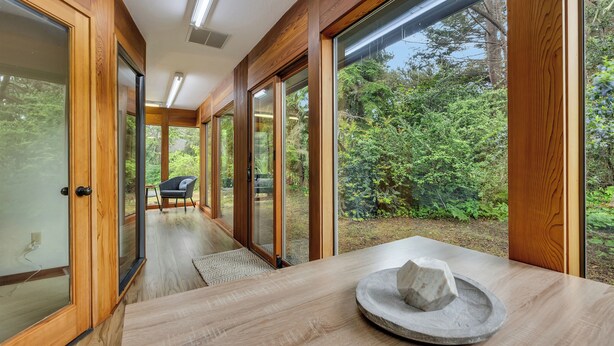 Un interior moderno con ventanas amplias, paredes de madera y una pieza central de piedra sobre la mesa.