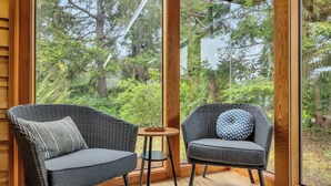 Una habitación con dos sillas de mimbre, una mesita redonda y un ventanal con vistas a árboles.