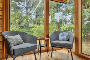 A room with two wicker chairs, a small round table, and a large window offering a view of trees.