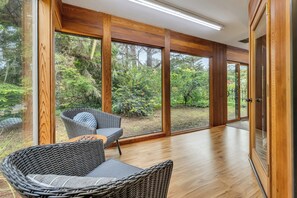 Un interior moderno con ventanas amplias, mobiliario de mimbre y suelo de madera.