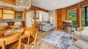 Un interior moderno con una mesa de comedor de madera, sillas, un sofá y un amplio ventanal con vistas a zonas verdes.