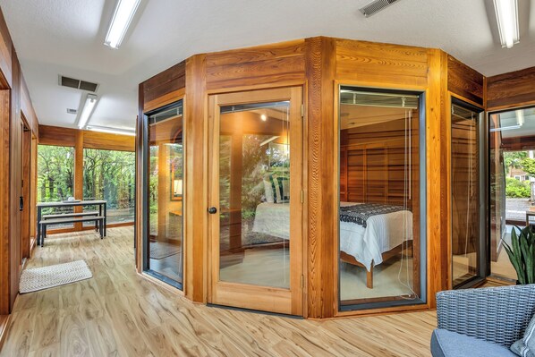 Un dormitorio en esquina con puerta corredera de vidrio, una cama, un banco y vistas al exterior.