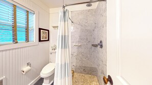 Ein Badezimmer mit Toilette, Dusche und einem Fenster mit Jalousien.