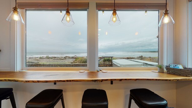 A bar area with a view of the beach, featuring a wooden counter and three black stools. - SURF SHACK at Seaside Beach- OCEAN FRONT - HOT TUB (Seaside)