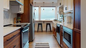 A modern kitchen with wooden cabinets, stainless steel appliances, and a view of the ocean through large windows. - SURF SHACK at Seaside Beach- OCEAN FRONT - HOT TUB (Seaside)