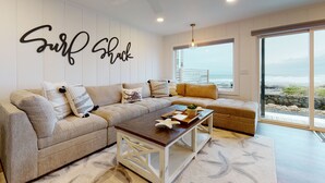 A modern living room with a large sectional sofa, a coffee table, and a wall-mounted sign that reads "Surf Shack". - SURF SHACK at Seaside Beach- OCEAN FRONT - HOT TUB (Seaside)