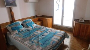 A bedroom with a bed, wooden headboard, a small wooden nightstand, a TV mounted on the wall, and a window with a view of the outside. - Small resin house (Arcachon)
