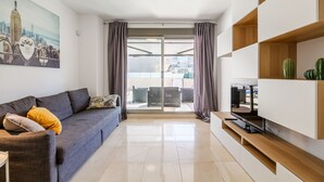 Una sala de estar moderna con un sofá gris, un televisor de pantalla plana sobre un soporte de madera y un cuadro de un paisaje urbano en la pared.