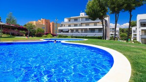 Una piscina de borde curvo, rodeada por un césped cuidado y árboles.